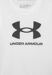 Camiseta de algodón blanca con un gran logo negro de Under Armour y texto debajo. El diseño es sencillo con un escote redondo.