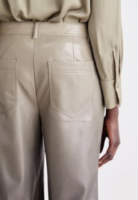 Beige faux læderbukser med en glat tekstur, der har to baglommer og en tætsiddende talje, kombineret med en lys grøn bluse.
