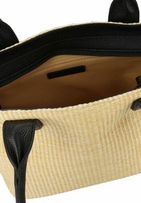 Sac tote en paille tissé avec des poignées en cuir noir. L'intérieur dispose d'une poche zippée et d'une doublure en tissu beige.
