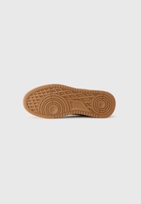 Tan rubber shoe sole with circular and diamond-patterned textures, featuring a raised edge and prominent tread for grip.