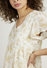 Robe en tissu léger avec un motif floral dans des couleurs pastel. Présente un décolleté en V et des manches volantées avec une taille froncée.