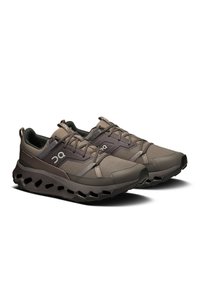 Baskets de sport marron foncé avec tige en mesh, embout renforcé, système de laçage et semelle rembourrée dotée de trous de ventilation pour la respirabilité.