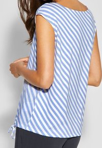 Randig skjorta i blå och vit bomull, har en avslappnad passform, korta ärmar och en sidoknytning vid nederkanten.