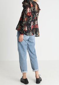 Zwarte bloemenblouse met ruches aan de mouwen, meerkleurig bloemenpatroon, gecombineerd met lichtblauwe opgerolde jeans en zwarte plateau schoenen.