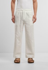 Ľahké nohavice smotanovej farby s textúrovaným vzorom, elastickým pásom a šnúrkou; v kombinácii s hnedými sandálmi na slip-on.