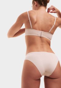Lichtbeige bh met verstelbare banden en een haak-en-oogsluiting; gecombineerd met bijpassende naadloze bikini-slipjes, gladde textuur.