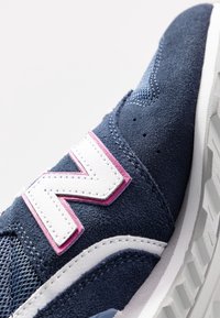Marinblå sneakers som har material av mocka och mesh, vita accenter, en framträdande rosa och vit "N"-logotyp samt en texturerad vit sula.