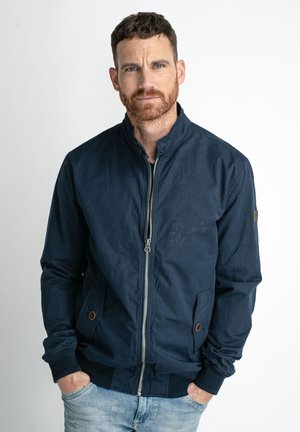 Marine bomberjakke i let stof med ståkrave, frontal lynlås og to sidelommer. Ribkanter ved ærmerne og nederste kant. Minimale designdetaljer.