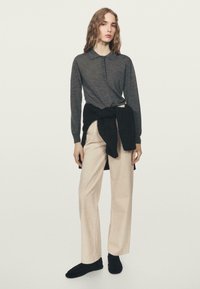 Długorękawowa, ciemnoszara koszulka polo z trzema guzikami, zestawiona z kremowymi, szerokimi spodniami. Czarny sweter przewiązany w talii. Czarne obuwie.