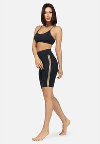 Czarny sportowy stanik z złotym wykończeniem oraz pasującymi szortami z wysokim stanem, które mają złotą paski po boku, wykonane z elastycznego materiału.