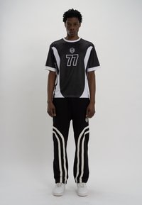 Camisola preta e branca de mangas curtas com o número 77 e logótipo; emparelhada com calças pretas com riscas laterais brancas e sapatilhas brancas.