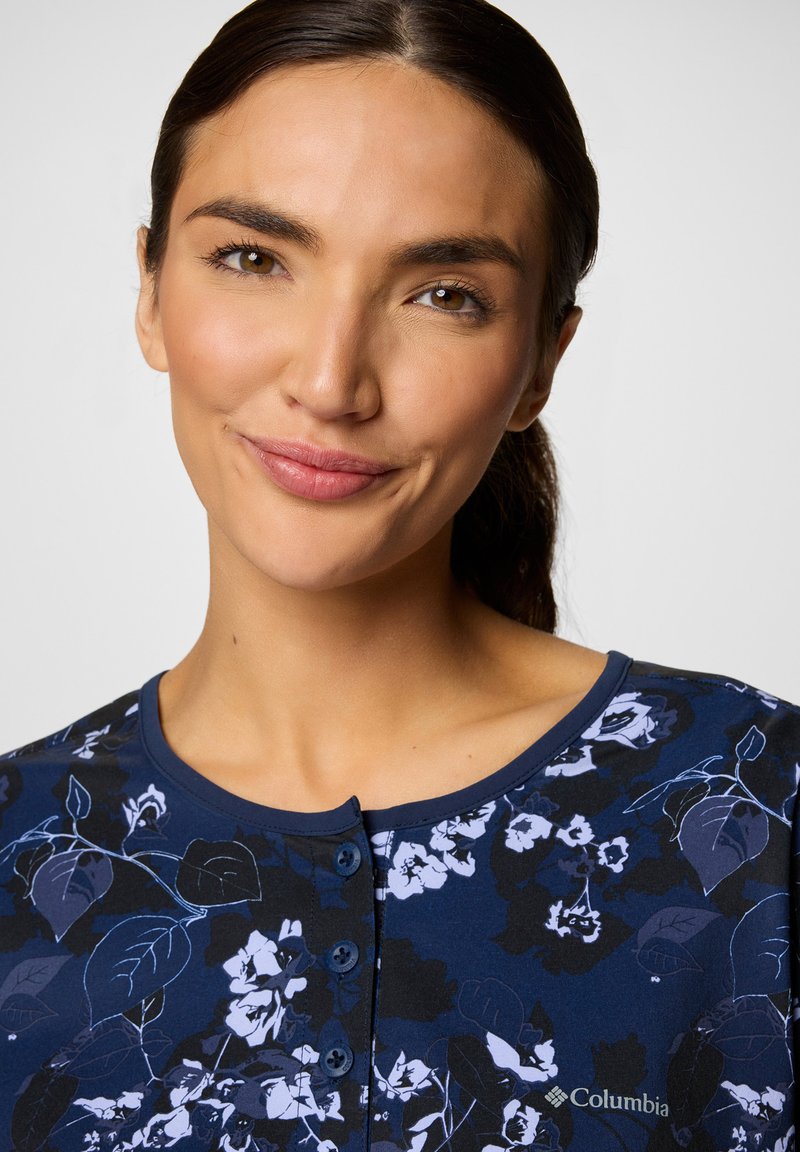 Navy-blaues Blusenshirt mit rundem Ausschnitt, kurzen Ärmeln und Knopfleiste. Hat weiße und lila Blumenmuster auf weichem Stoff.