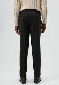 Donkerbruine, op maat gemaakte broek met een rechte pijp, een gladde textuur en twee achterzakken. Gecombineerd met een licht geribde trui en schoenen.