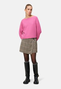 Pull rose côtelé à large encolure, associé à une jupe portefeuille à carreaux avec un détail de bouton. Bottes en caoutchouc noires montantes complètent la tenue.