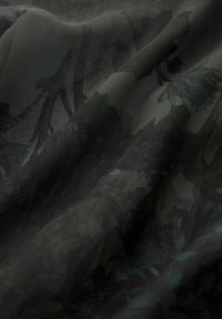Durchscheinender schwarzer Stoff mit einem filigranen Blumenmuster in Dunkelgrün und Grau, der eine leicht strukturierte Oberfläche und einen fließenden Fall aufweist.