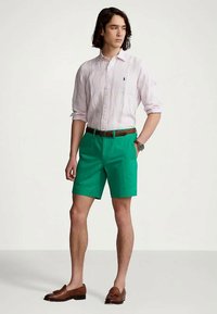 Green cotton shorts paired with a light pink striped shirt. Accessories include a brown belt and loafers. Simple design, casual fit.