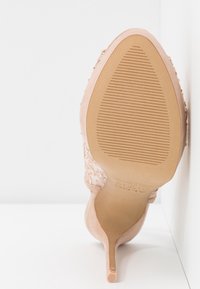 Jasnoróżowy but na wysokim obcasie z teksturowaną cholewką i spiczastym noskiem, z rowkowaną gumową podeszwą zapewniającą przyczepność.