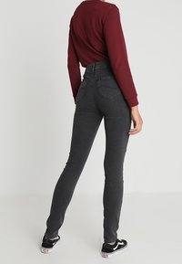 Jeans de tiro alto en gris, fabricados en denim, con un ajuste slim, bolsillos traseros y combinados con zapatillas de deporte en blanco y negro.