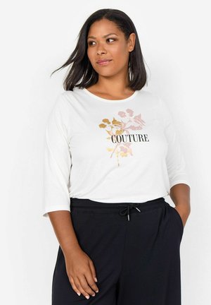Un top alb cu mânecă lungă, având textul "COUTURE" în negru, cu un design floral în auriu și roz. Asortat cu pantaloni negri cu șnur.