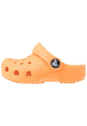 Pomarańczowe chodaki wsuwane z otworami wentylacyjnymi i regulowanym paskiem z tyłu, z czarnym okrągłym logo z boku.