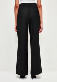 Pantalons larges noirs avec une texture lisse, taille haute et une poche arrière unique. Pr ésente un design ajusté et une silhouette classique.
