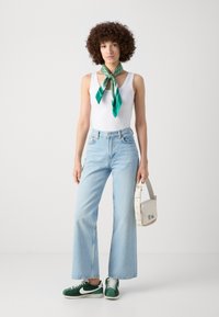 Light blue high-waisted flared jeans, white tank top, green and teal silk scarf tied at the neck, green sneakers, and a white crossbody bag.