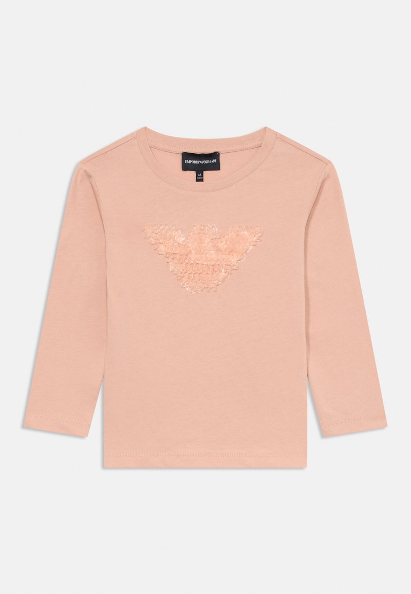 Chemise rose à manches longues en coton doux, présentant un logo texturé et brillant au centre. Design simple, col rond et ourlet droit.