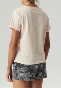 Jasnoróżowa koszulka z krótkim rękawem z podwiniętymi mankietami, w połączeniu z ciemnymi szortami z białymi wzorami liści. Gładka, bawełniana tkanina.