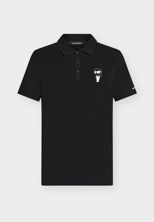 Polo noir à manches courtes avec trois boutons et un petit personnage de dessin animé blanc portant des lunettes de soleil brodé sur la poitrine gauche.