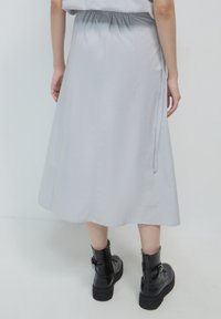 Persona che indossa una gonna midi grigia chiara con cintura elastica e stivali alla caviglia con platform neri, in piedi di fronte a uno sfondo neutro.