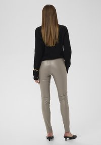 Pull en maille noire associé à des leggings en simili cuir beige. Texture lisse et ajustée ; le modèle porte des mules à talons noires. Design simple et minimaliste.