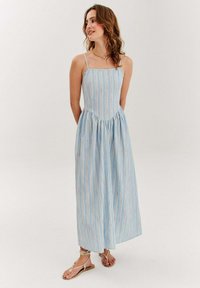 Jasnoniebieska sukienka maxi w paski z cienkimi ramiączkami, dopasowaną talią i rozkloszowaną spódnicą. Materiał ozdobiony jest cienkimi, kolorowymi paskami.