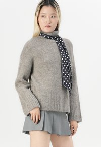 Gray knitted sweater with a turtleneck, featuring long sleeves and ribbed hem. Paired with a gray pleated skirt and a black polka dot scarf.