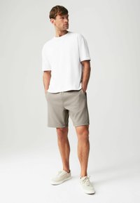Camiseta blanca de manga corta, pantalones cortos grises y zapatillas ligeras. Diseño simple, corte relajado, textura suave y pantalones cortos hasta la rodilla.