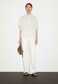 Lys grå stribet top med høj krave, trykknapper, hvide vide bukser, brun taske og brune sandaler. Glat, afslappet stof.