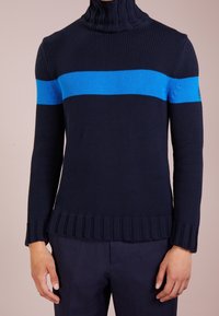 Pullover a maglia di colore blu navy con colletto alto e una striscia orizzontale di un blu brillante. Orlo e polsini a costine, tessuto testurizzato, design aderente.