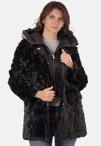 Cappotto in finta pelliccia nera con colletto removibile e voluminoso, dotato di chiusura con zip e bottoni. La texture è soffice con una fodera interna lucida.