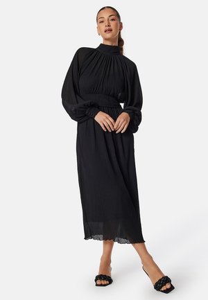Abito nero a maniche lunghe con collo alto, design plissettato e vita elasticizzata. Il tessuto trasparente presenta una silhouette fluida e un orlo a scollatura.