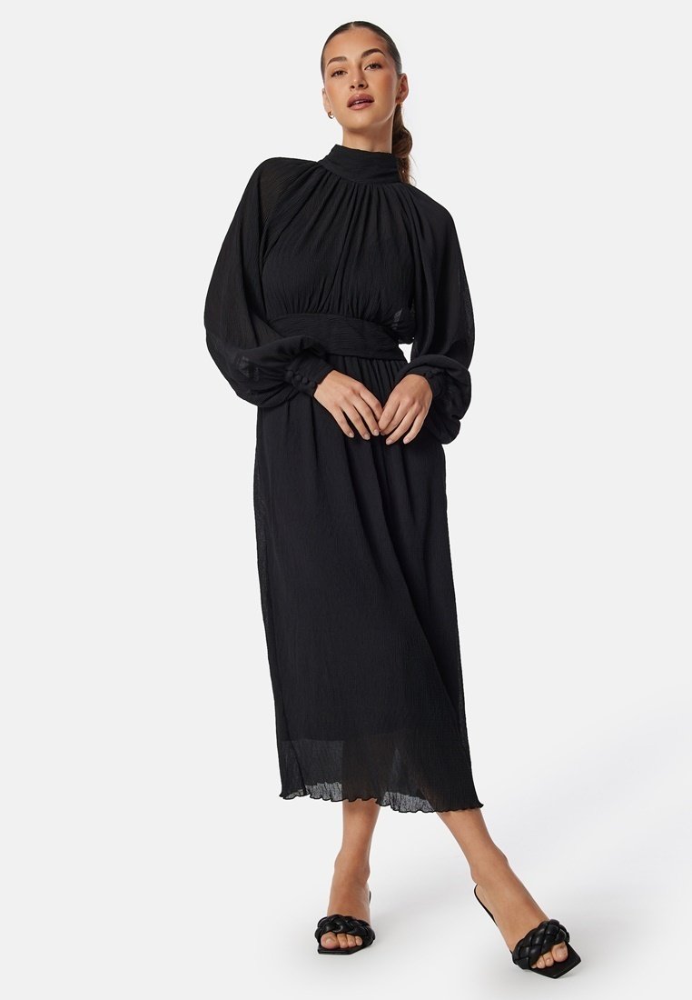 Robe noire à manches longues avec un col haut, un design plissé et une taille élastique. Le tissu transparent présente une silhouette fluide et un ourlet en forme de vagues.