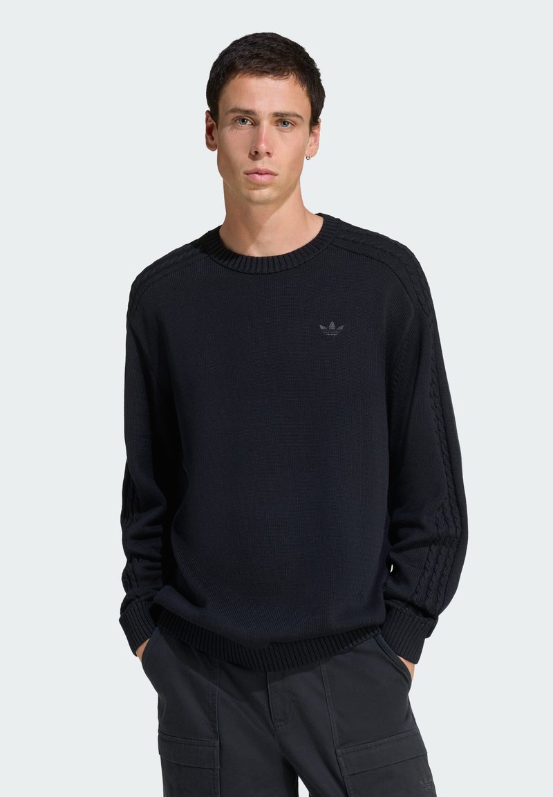 Sweater preto de malha com gola redonda canelada e painéis laterais texturizados. Pequeno logótipo no peito, combinado com calças cargo escuras.