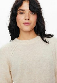 Svetlobežová svetrová mikina s okrúhlym výstrihom, raglanovými rukávmi a jemnou textúrou. Tkanina vyzerá pletená a je mierne priehľadná.