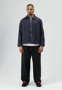 Donkerblauwe katoenen jas met kraag en knopen aan de voorkant, gecombineerd met losse zwarte spijkerbroek en zwarte platformschoenen met roze veters.