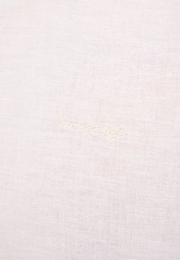 Jasny materiał o subtelnej teksturze, z wyszywanym tekstem w stylu kursywy. Cały design jest minimalistyczny i delikatny.