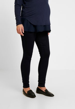 Camiseta de manga larga azul marino superpuesta sobre un dobladillo acampanado, combinada con jeans skinny oscuros y zapatos sin cordones negros para un look casual y ajustado.