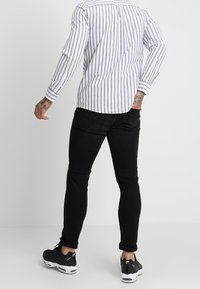 Gestreepte blouse met lange mouwen in wit en marineblauw, met een knoopsluiting op de achterkant van de hals, gecombineerd met zwarte slim-fit jeans en zwarte sneakers.