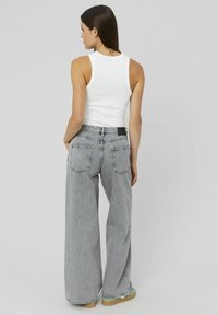 Jean en denim gris à jambe large et taille haute, comportant deux poches arrière et un rivet noir à la ceinture. Associé à un débardeur blanc.