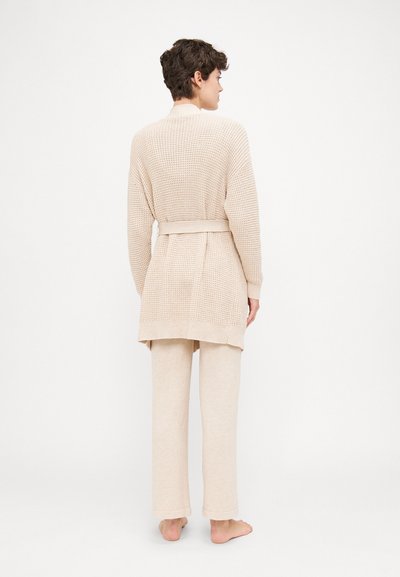Beige knit cardigan with a tie belt, featuring a textured pattern and long sleeves, paired with matching lightweight trousers.