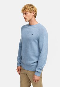 Lyseblå strikkegenser med ribbede mansjetter og kant, rund hals og subtilt logo-detail på brystet. Jevn tekstur og klassisk passform.