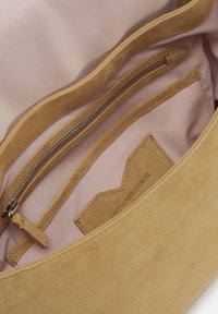 Beiges Wildleder-Innenfutter einer Handtasche mit weichem rosa Innenfutter, ausgestattet mit einer Reißverschlusstasche und einem etikettierten Lederanhänger.
