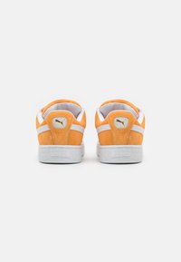 Orange suede sneakers with white accents, featuring a textured rubber sole and a small gold logo on the back.